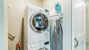 A compact laundry area with a front-loading washer and dryer, a fire extinguisher, and a towel rack.