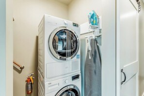 A compact laundry area with a front-loading washer and dryer, a fire extinguisher, and a towel rack.