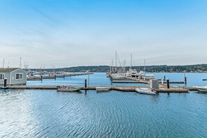 A marina with boats docked at piers, a small building on the left, and a calm water body.