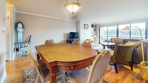 A dining area with a wooden table and chairs, a chandelier, and a sofa set in a bright room with large windows. - 2 BR condo with stunning water views (Port Ludlow)