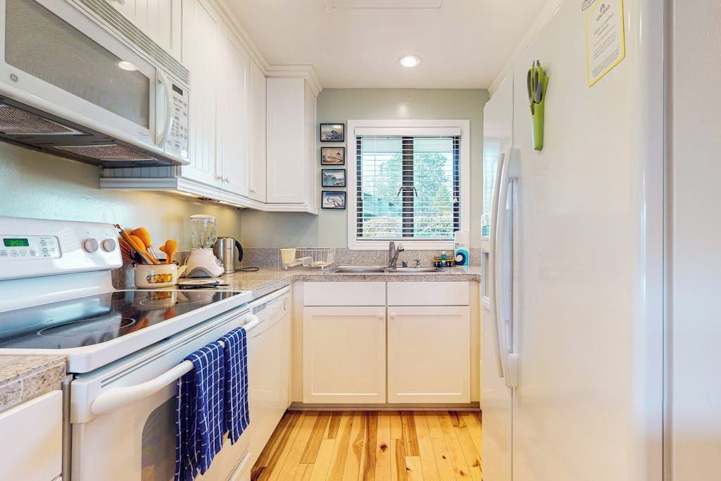 A compact kitchen with white cabinets, a microwave, an oven, and a sink.