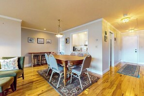 Un coin repas avec une table et des chaises en bois, un tapis, et une cuisine en arrière-plan.
