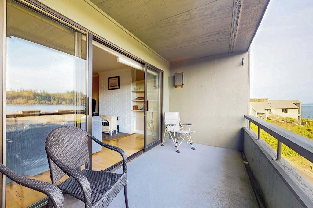 A balcony with a wicker chair, a white chair, and a small table.