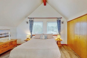 A bedroom with a large bed, two bedside tables, a wardrobe, and a sloped ceiling. - 2BR Oceanview Dog Friendly - Fireplace - Deck (Pacific Beach)