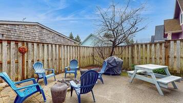 A backyard with a wooden fence, outdoor seating including chairs and a table, and a barbecue grill.