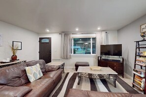 A living room with a leather sofa, a coffee table, a television, and a bookshelf. - Charming 3BR - Hot Tub - Gas Grill - Dogs-OK (Port Orchard)