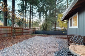 A gravel patio with stepping stones, a wooden fence, and a building with a window. - Charming 3BR - Hot Tub - Gas Grill - Dogs-OK (Port Orchard)