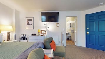 A hotel room with a bed, a desk, a chair, a TV, and a blue door.