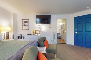 A hotel room with a bed, a desk, a chair, a TV, and a blue door. - 1BR Hotel Room right in Downtown Port Townsend (Port Townsend)