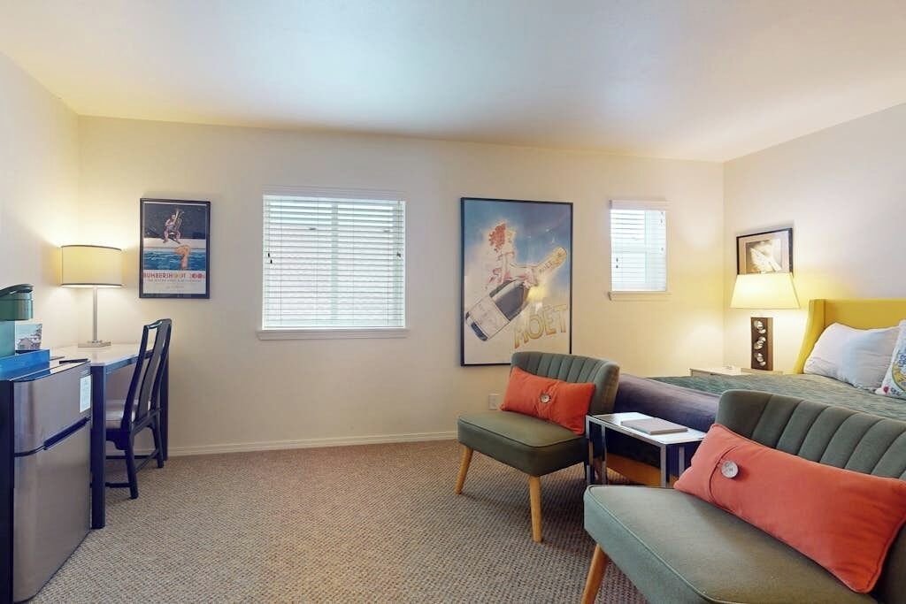 A hotel room with a desk, two chairs, a sofa, and a bed. There are three framed pictures on the walls.