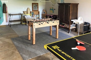 Een kamer met een tafelvoetbaltafel, een pingpongtafel en een boekenplank.