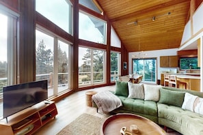 A spacious living room with a large flat-screen TV, a green sofa, and a wooden coffee table. - 1BR  with loft retreat with wrap around balcony & Washer Dryer (Westport)