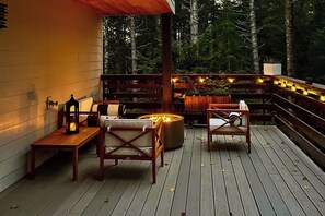 Eine Terrasse im Freien mit Holzmöbeln, einem Feuerkorb und Lichterketten.