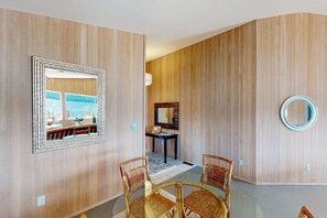 Une pièce avec un mur lambrissé en bois, un miroir rond et un coin repas avec des chaises en osier.
