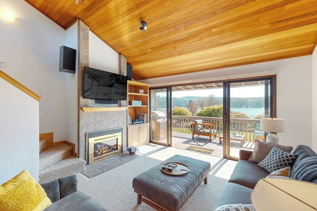 A modern living room with a fireplace, a television, and a balcony with a view.