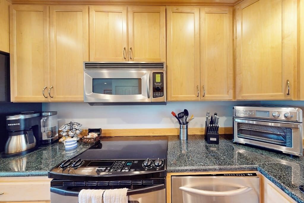 A kitchen with wooden cabinets, a stainless steel microwave, a gas stove, a coffee maker, and a toaster oven.