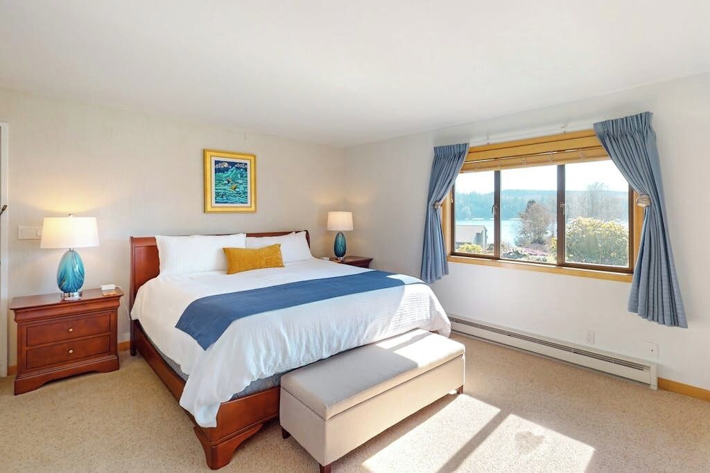Un dormitorio con cama, mesitas de noche, una ventana con cortinas y vistas al exterior.