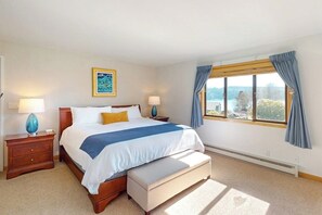 A bedroom with a bed, bedside tables, a window with curtains, and a view of the outdoors.