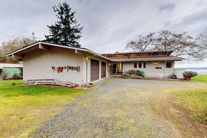 Une maison à deux étages avec un garage, une véranda et une allée gravillonnée.