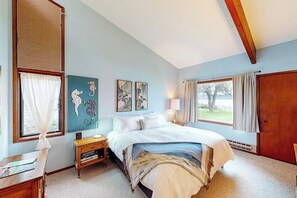 Un dormitorio con cama, mesitas de noche, un ventanal con cortinas y una obra de arte en la pared.
