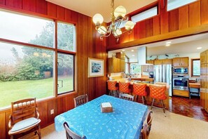 Un coin repas avec une table dressée pour quatre personnes, une cuisine équipée d’appareils modernes et une grande fenêtre donnant sur l’extérieur.