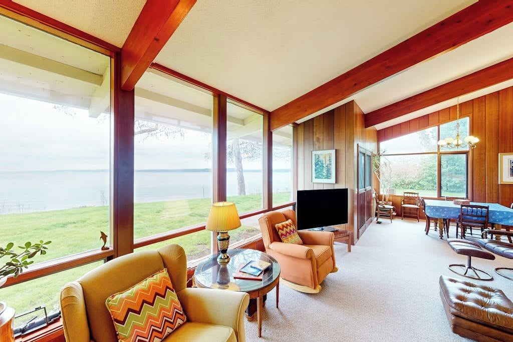 A spacious living room with a large window overlooking a grassy area, a television, and a dining area with wooden furniture.