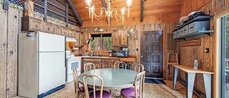A wooden interior with a dining table, chairs, a refrigerator, and a kitchen area.