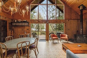 A wooden interior with a dining area, chairs, a table, a fireplace, and large windows. - Dreamy 2BR Dog Friendly - Pool - Hot Tub - Dock (Shelton)