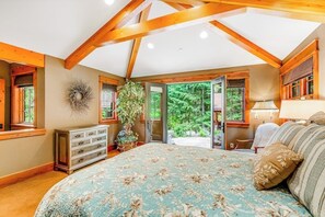 Ein Schlafzimmer mit einem großen Bett, Holzbalken, einem Schminktisch, einer Pflanze und Blick ins Freie.