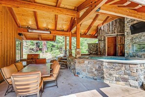 Een overdekt buitengebied met een stenen openhaard, een hottub en een eettafel met stoelen.