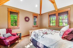 Ein Schlafzimmer mit einem Bett, einem Sessel und zwei Fenstern mit Holzrahmen.
