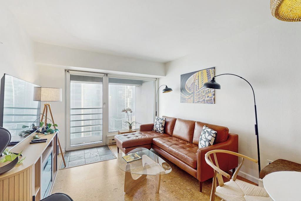 A modern living room with a leather sofa, a glass coffee table, and a desk with a lamp.