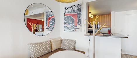 Un espacio habitable moderno con una mesa de comedor redonda, un sofá con cojines estampados y una cocina visible a través de un vano abierto.