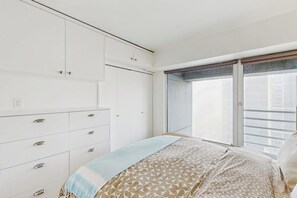 Ein Schlafzimmer mit Bett, Kommode und einem Fenster mit Blick auf Gebäude.