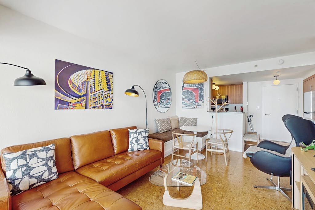 A modern living room with a brown leather sofa, a glass coffee table, and a dining area with a white table and chairs.