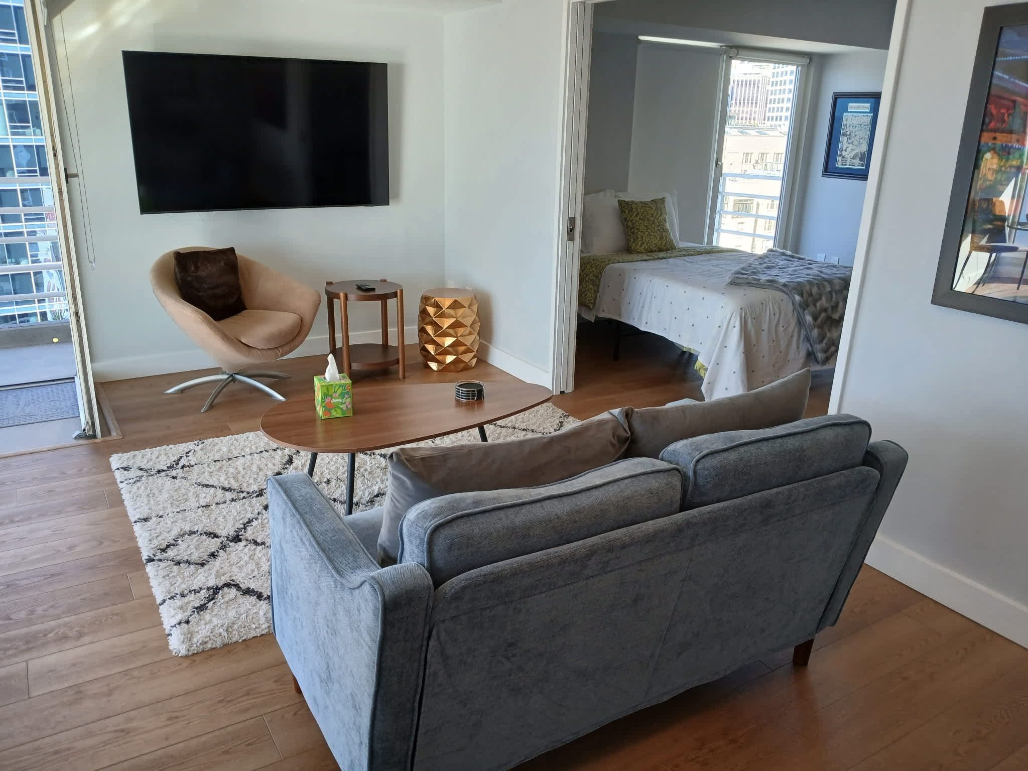 A modern living room with a grey sofa, a small wooden coffee table, and a TV mounted on the wall.