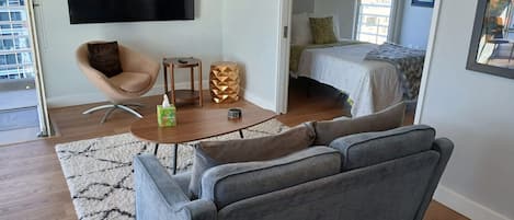 Uma sala de estar moderna com um sofá cinzento, uma mesinha de centro de madeira e uma TV fixada na parede.