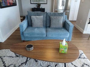 A living room with a blue sofa, a wooden coffee table, and a patterned rug. - 2BR condo with water view, full kitchen, Washer Dryer (Seattle)