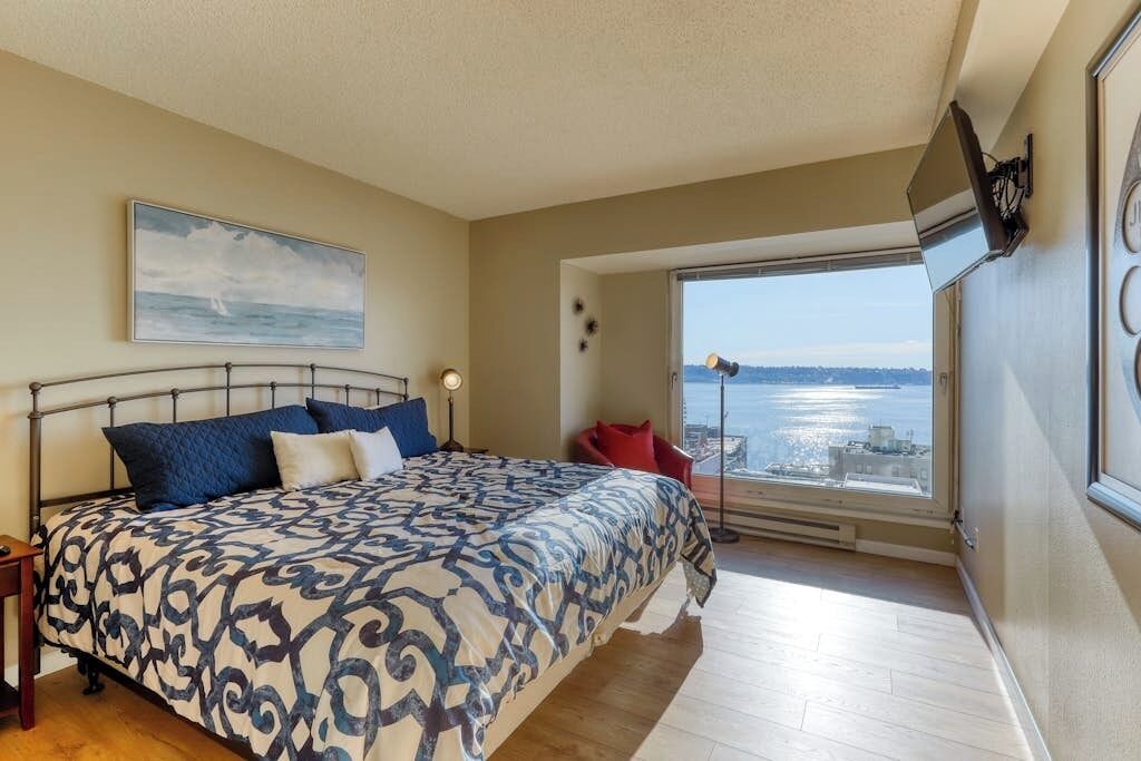 Une chambre à coucher avec un lit, une fenêtre donnant sur un beau paysage, un fauteuil rouge et un tableau accroché au mur.