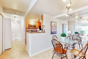 A modern kitchen with a central island, a dining area with a glass table and wooden chairs, and a hallway leading to another room. - Luxe 1BR with huge bay view, pool, & hot tub (Seattle)
