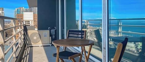 Un balcón con mesa y sillas, un ventilador y vistas a un puente y al paisaje urbano.
