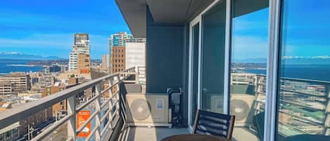 Varanda com mesa e cadeiras, vista para um horizonte urbano com edifícios e um corpo d'água.