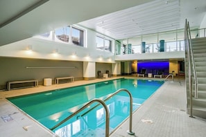 An indoor swimming pool with a clear view of the sky through large windows, a staircase, and lounge chairs. - Luxe 1BR with huge bay view, pool, & hot tub (Seattle)