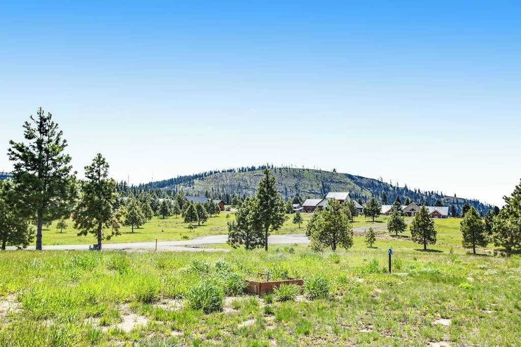 A rural landscape with a hill, trees, and a few buildings in the distance.