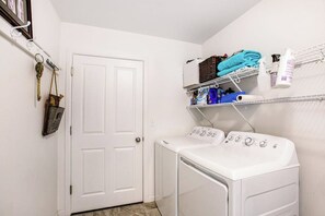 Une buanderie équipée d’un lave-linge et d’un sèche-linge à chargement frontal, d’une étagère avec des serviettes pliées et d’une porte sur laquelle est accrochée une clé au mur.