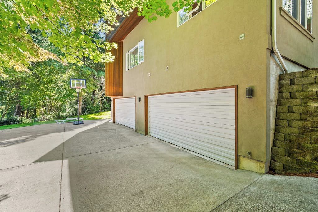 Un immeuble résidentiel doté de deux portes de garage, d’un panier de basketball et d’un mur en pierre.