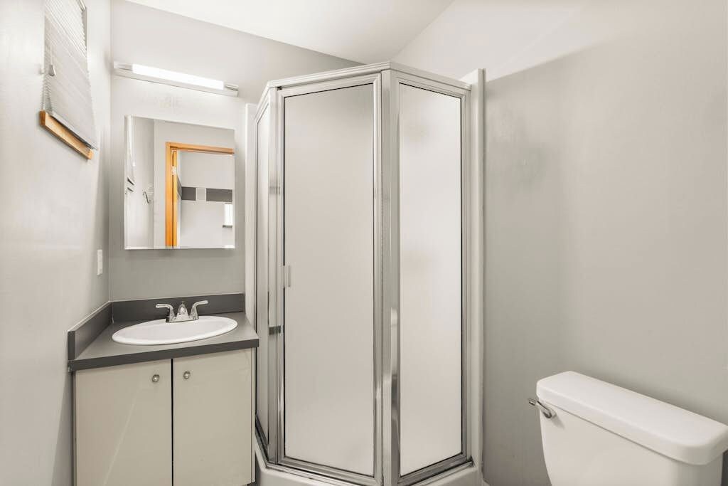 A bathroom with a shower enclosure, a sink, and a toilet.