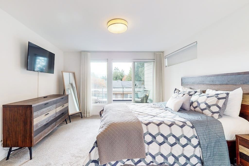 Une chambre à coucher avec un lit, une commode, un téléviseur et une fenêtre avec des rideaux.