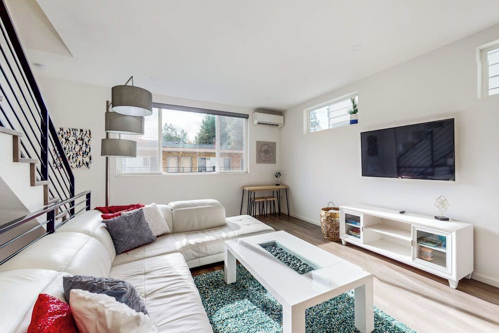 A modern living room with a white sofa, a coffee table, a TV, and a staircase.