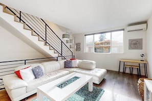 A modern living room with a white sectional sofa, a coffee table, and a staircase with black railings. - 3 BR townhome with rooftop deck and city access (Seattle)